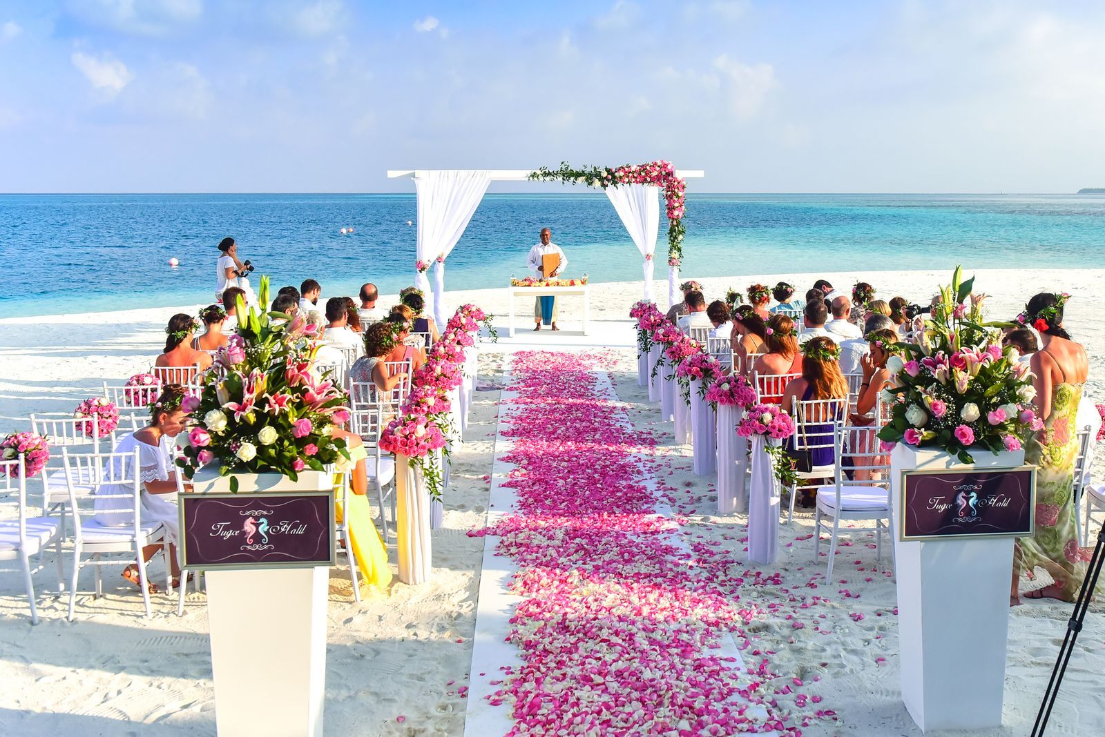 Beach wedding ceremony with guests seated along a petal-strewn aisle facing the sea, the kind of celebration wedding cruises bring ashore