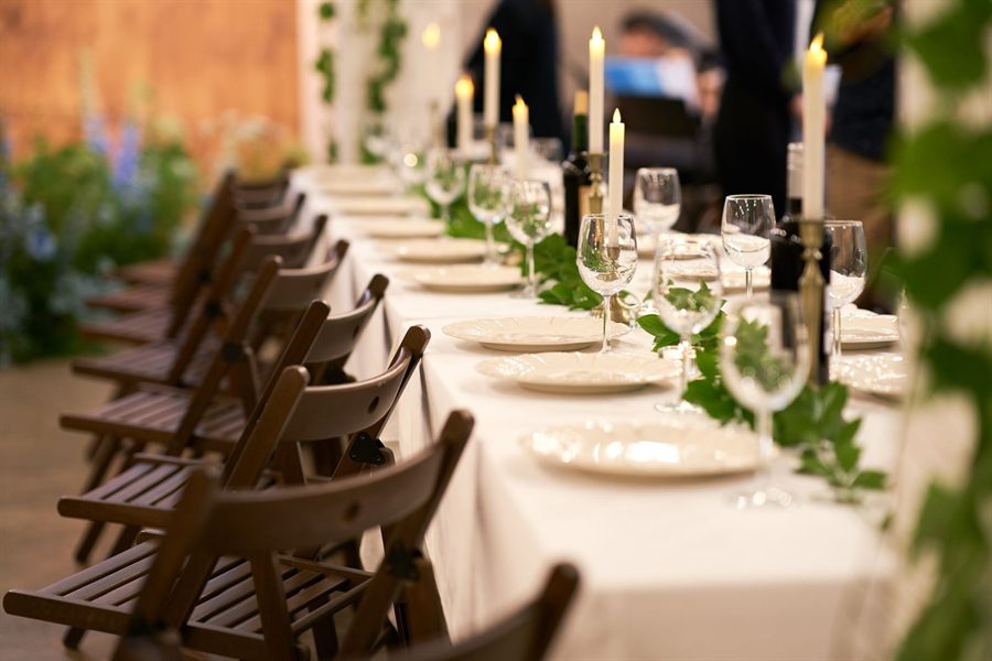 Long banquet table set with candles, glassware and greenery for a wedding dinner