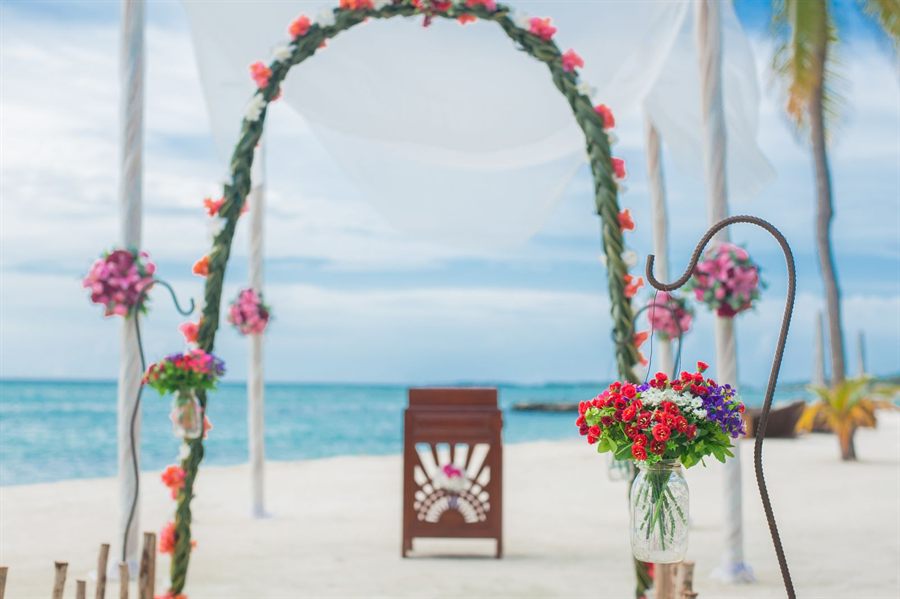 Flower-covered wedding arch on a white-sand beach with turquoise water behind
