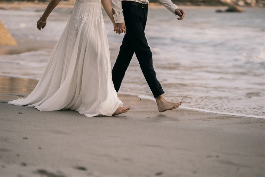 Bride and groom walking barefoot along the water's edge