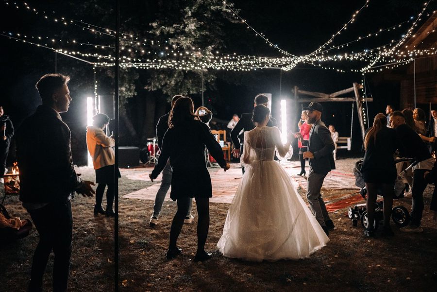Wedding guests dancing under string lights at an evening reception