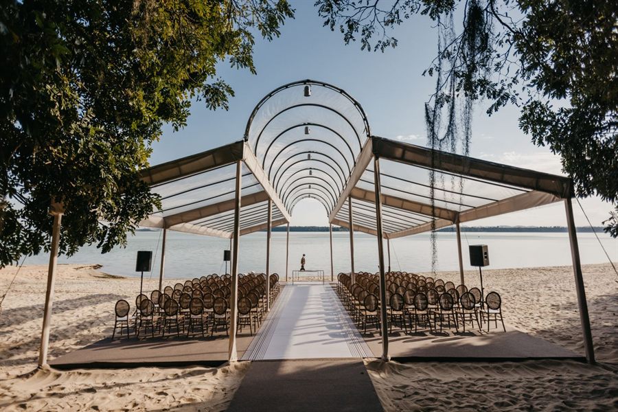 Open-air beachfront wedding pavilion with rows of chairs under the trees
