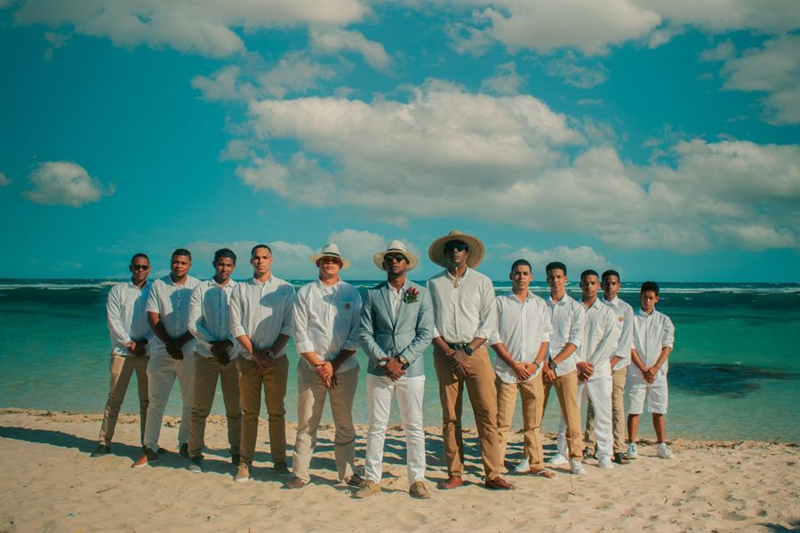 Groom and groomsmen in light summer clothes lined up on a tropical beach